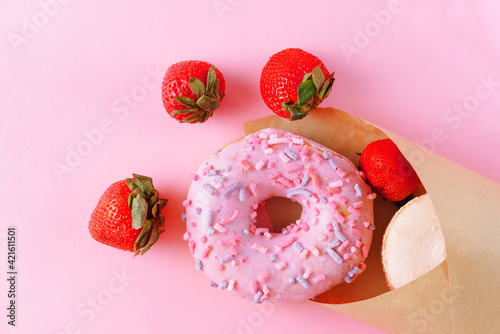 donat, fresh strawberries, paper bag on pink background top view