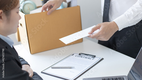 Employee handed over a document envelope and a box of work equipment beside him, Businessman submits resignation documents to their supervisor and take personal equipment in a brown box. © Puwasit Inyavileart