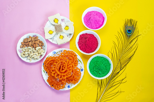 Colorful holi powder or gulal in ceramic bowl along with traditional Indian sweet food imarti, sandesh, cashew and almonds in plate on multicolor background. photo