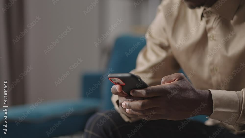 young black man is using smartphone at home, browsing internet sites, viewing social nets,closeup view of hands