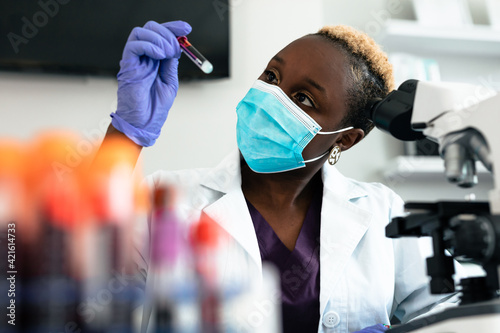 Black female scientist in mask in laboratory with test tubes and microscope equipment