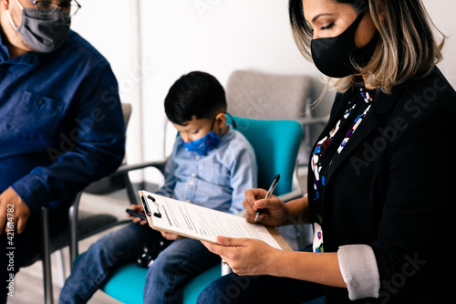Latino family wearing masks completing medical forms in doctor office
