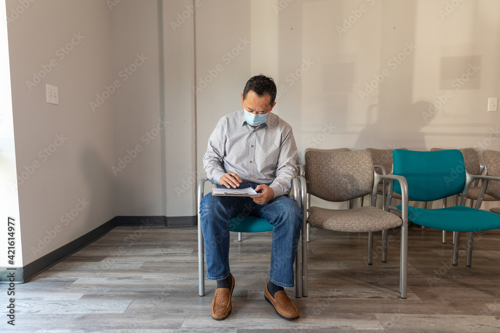 Asian man filling out patient forms at doctors office waiting area Asian man filling out patient forms at doctors office waiting area