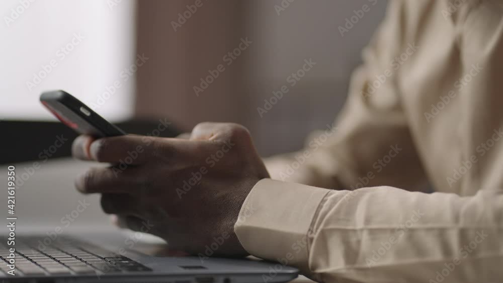 office worker is using smartphone at working place, checking social nets during work, closeup of hands of black man