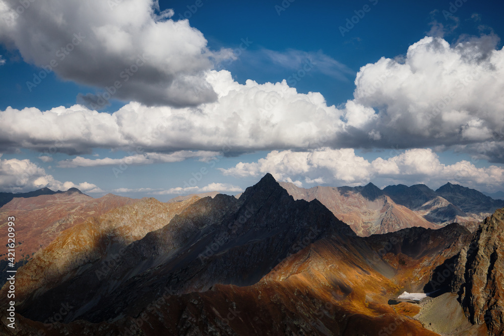view of an impressive mountain landscape in autumn, sharp peak, sheer cliff, mountain valley and a beautiful cloudy sky on the horizon, Caucasus, Russia