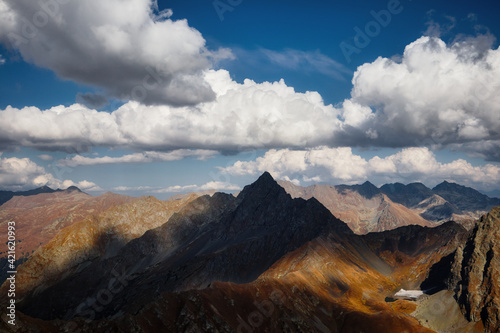 view of an impressive mountain landscape in autumn, sharp peak, sheer cliff, mountain valley and a beautiful cloudy sky on the horizon, Caucasus, Russia © ASHarchenko