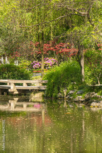 Suzhou, China - May 3, 2010: Humble Administrators Garden. Portrait of park corner with green water pond and green and red foliage in combination with pink flowers.