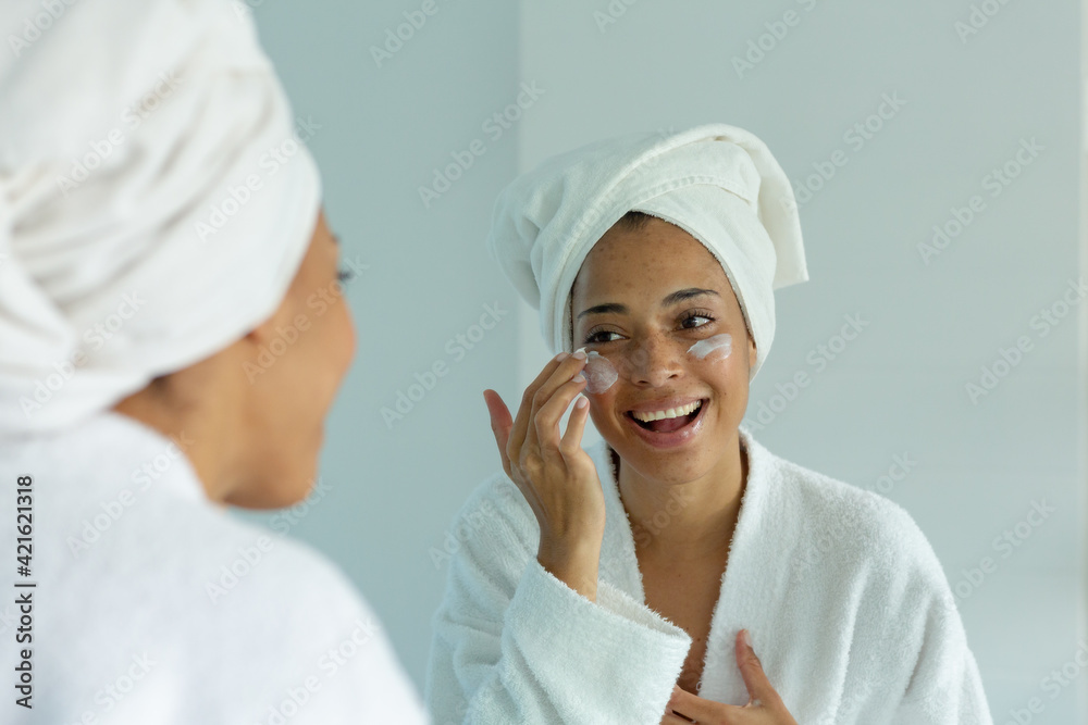 Mixed race woman wearing bathrobe and cleansing face mask in bathroom Mixed race woman wearing bathrobe and cleansing face mask in bathroom