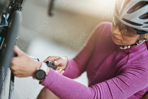 Professional female cyclist wearing protective helmet and glasses looking focused, using pump for inflating the tire of her bicycle, kneeling outdoors on a daytime