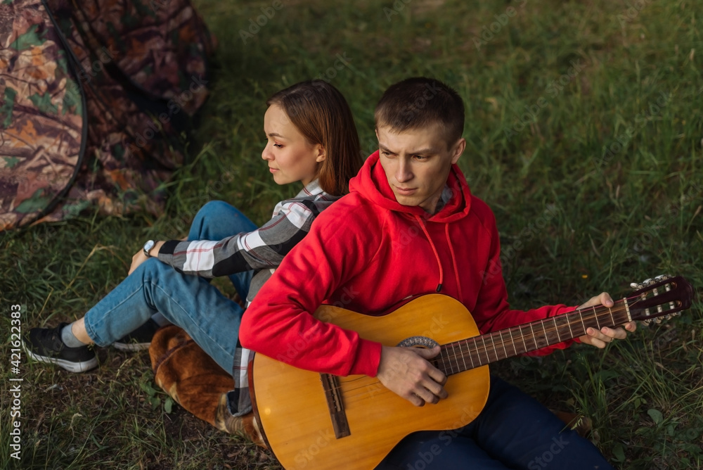 a young couple in love on the background of a campfire with a guitar. tourists on a picnic with music