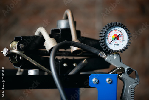 Tire inflation gun with pressure gauge and car jack on the rack of car fitting service background.