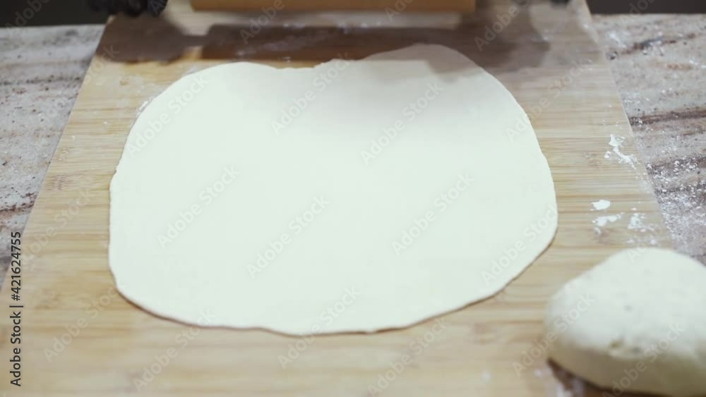 Una mujer con guantes negros en la cocina usando un rodillo de madera para amasar y estirar una masa de pizza en una tabla de madera. Concepto de hacer pizza casera y artesanal en casa