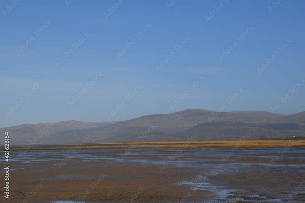 the smooth wet sand at the end of an estuary with the mountains in the background the smooth wet sand at the end of an estuary with the mountains in the background