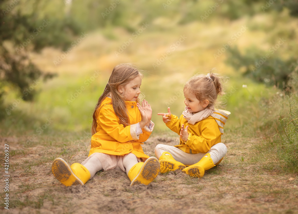 Two children playing in the forest. Happy sisters sitting and smiling in the park. Two children playing in the forest. Happy sisters sitting and smiling in the park.