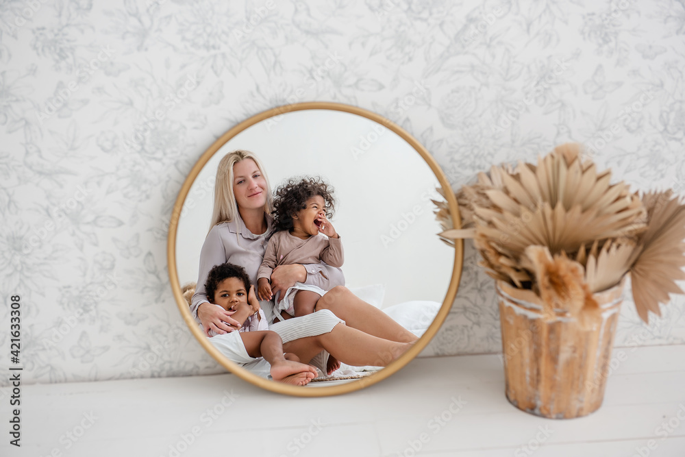 In round gold mirror, young blonde Caucasian mother sitting on wooden ...