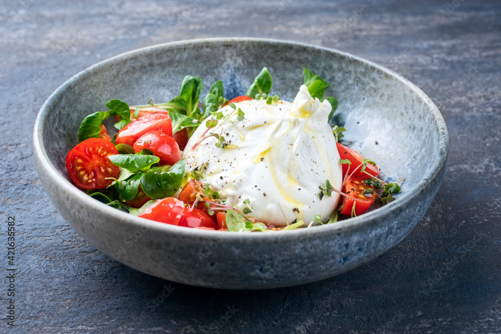 Modern style Italian Apulia Burrata cow milk cheese made from mozzarella and cream served with tomato and corn salad as close-up in ceramic Nordic design bowl Modern style Italian Apulia Burrata cow milk cheese made from mozzarella and cream served with tomato and corn salad as close-up in ceramic Nordic design bowl