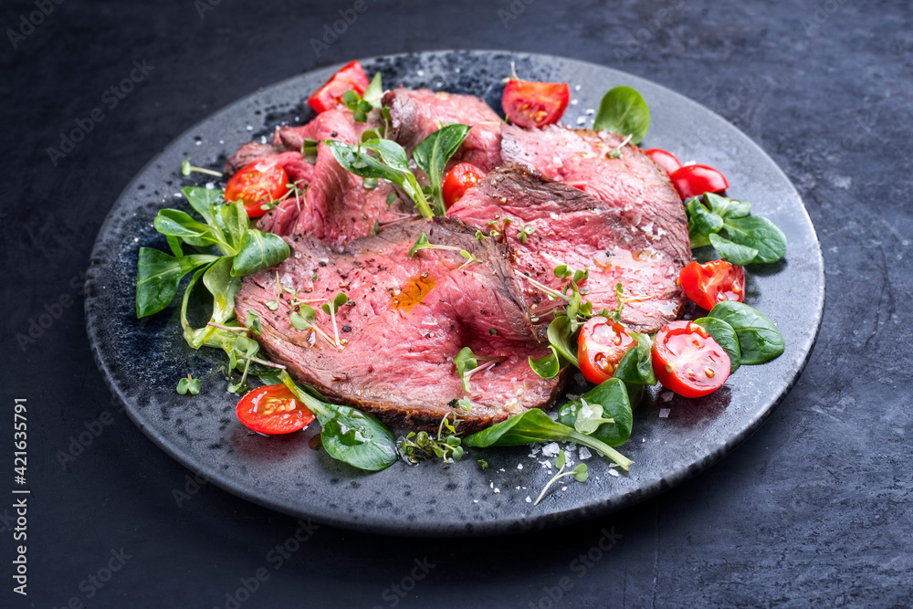 Modern style traditional Commonwealth Sunday roast with sliced cold cuts roast beef served with tomatoes and corn lettuce as close-up on a Nordic design plate with copy space Modern style traditional Commonwealth Sunday roast with sliced cold cuts roast beef served with tomatoes and corn lettuce as close-up on a Nordic design plate with copy space