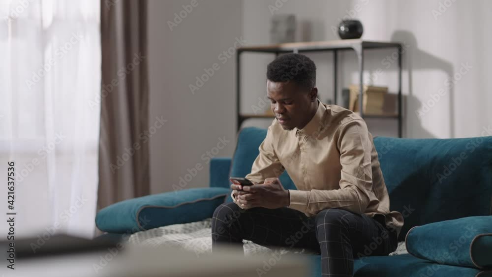 afro-american teenager is using smartphone, sitting at home alone, young black guy is typing message and viewing social nets afro-american teenager is using smartphone, sitting at home alone, young black guy is typing message and viewing social nets