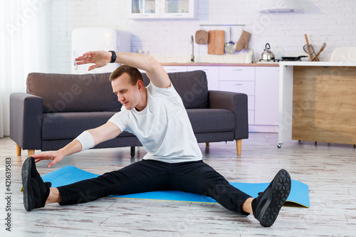 Muscular athletic man in a t-shirt doing warm-up exercises at home. Doing sports at home during the quarantine period. Fitness outside the gym