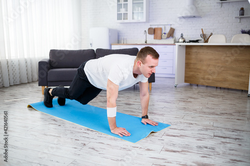Handsome muscular man in a t-shirt doing functional plank exercises on the floor at home. Fitness at home. Healthy lifestyle.