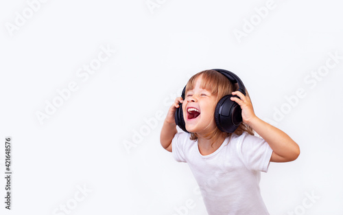 A little girl in big headphones with her mouth wide open sings a song.
