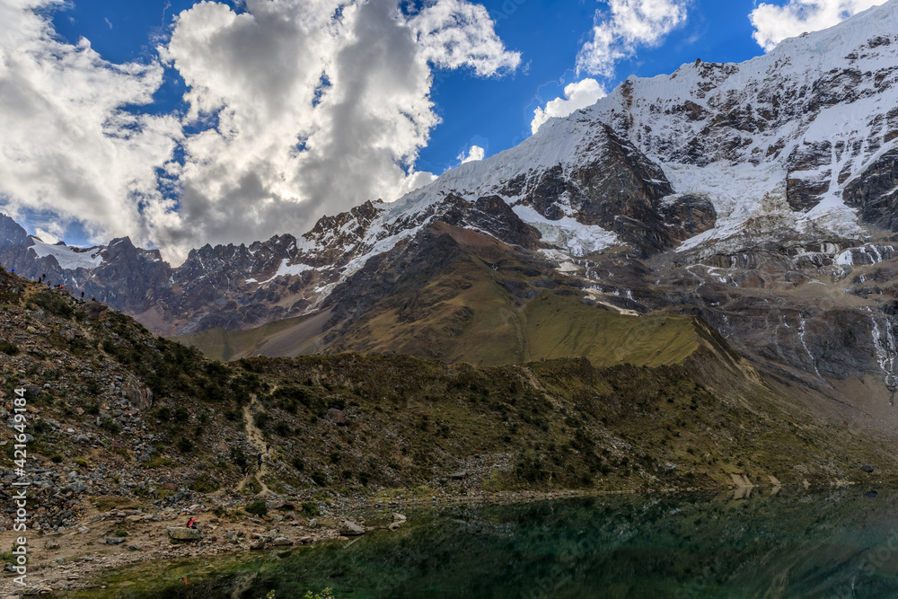 Panoramic view of the Humantay Lake at the base of the Salkantay mountain range in Peru, with its cold blue green waters calmly sitting under the snowy peak of the high altitude mountains Panoramic view of the Humantay Lake at the base of the Salkantay mountain range in Peru, with its cold blue green waters calmly sitting under the snowy peak of the high altitude mountains