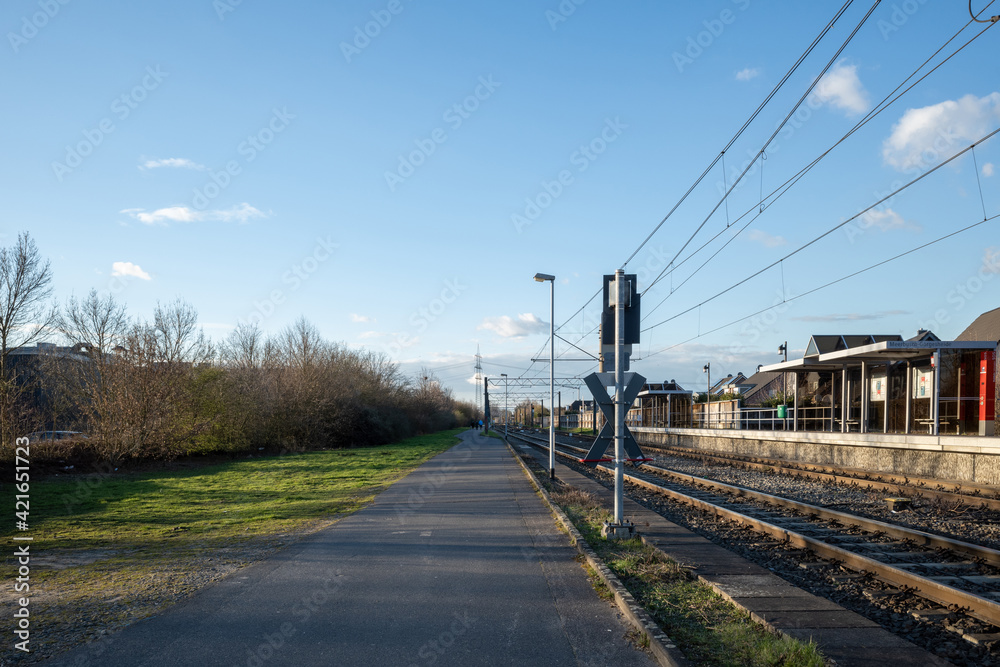 Outdoor sunny street view of narrow road along railway track and platform train station in Germany.