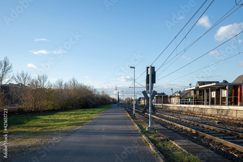 Outdoor sunny street view of narrow road along railway track and platform train station in Germany.