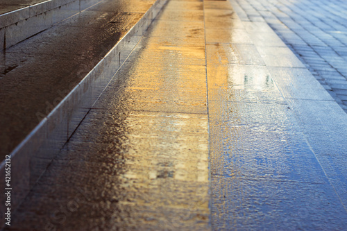 Wet granite stairs after rain on the street. City pattern with natural stone stairs and pavement. Colorful sunny background. 