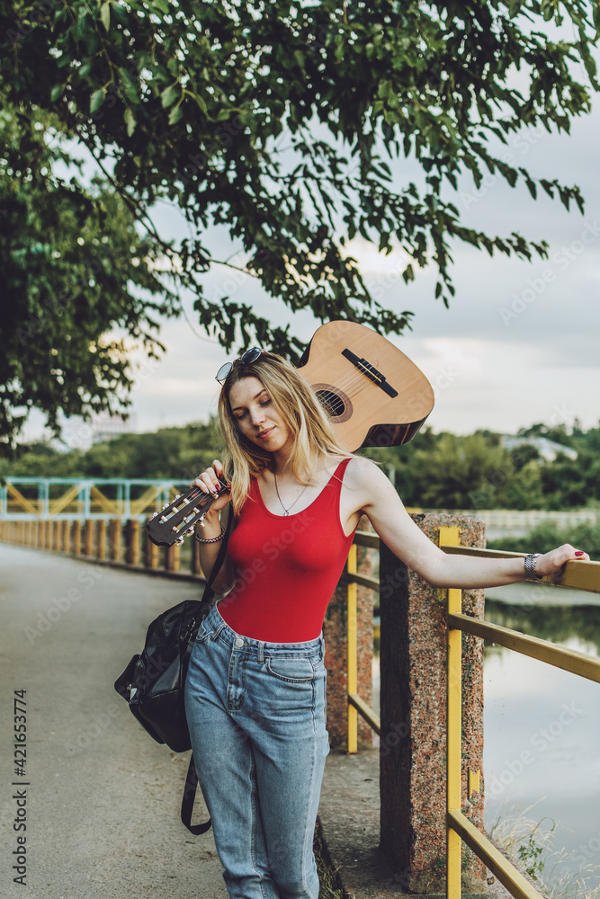 Beautiful blonde girl with guitar outdoor portrait. Young woman playing guitar in city street