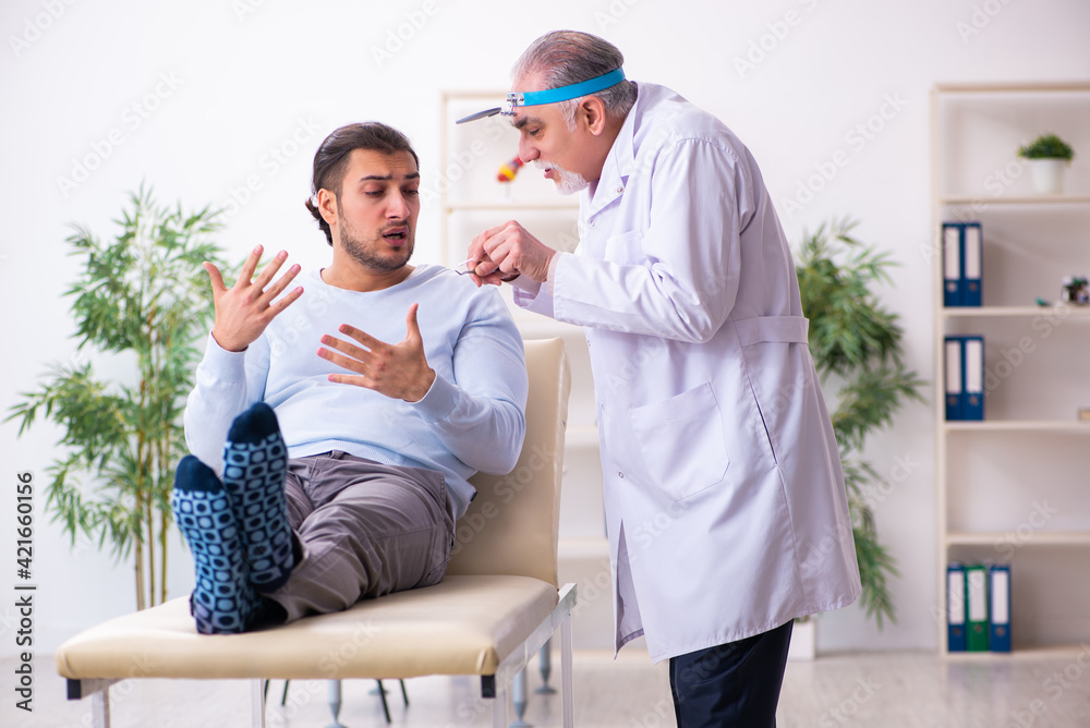 Fototapeta premium Young sick man visiting old doctor otolaryngologist
