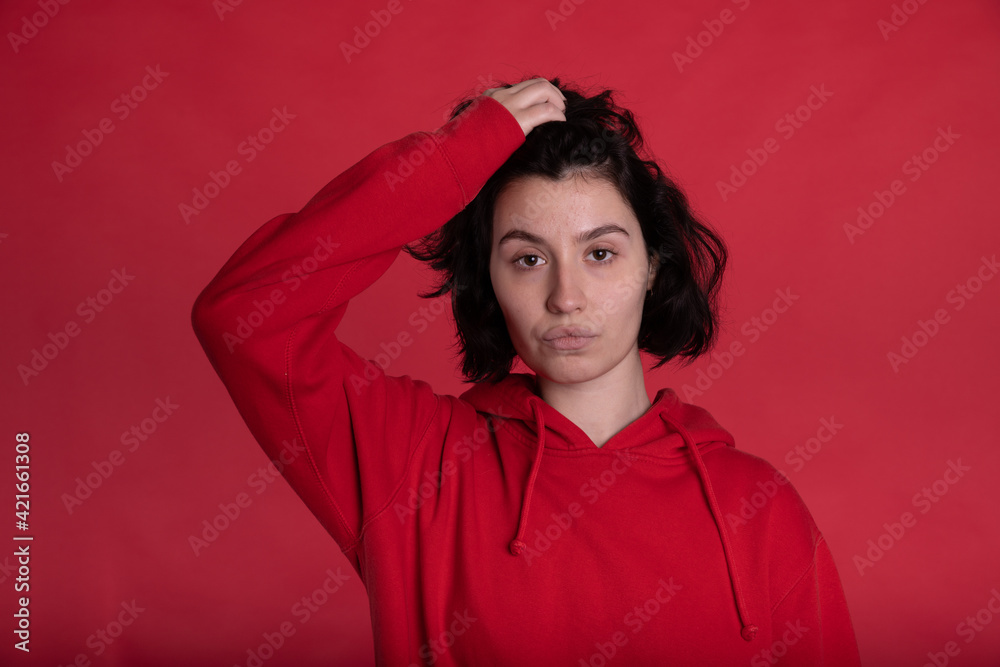 wild hair tired exhausted brunette Girl in red hoodie posing looking at camera duck lips on red studio backdrop copy space. Ads for psychologist, lowyer, consultant on sustainable relations concept wild hair tired exhausted brunette Girl in red hoodie posing looking at camera duck lips on red studio backdrop copy space. Ads for psychologist, lowyer, consultant on sustainable relations concept