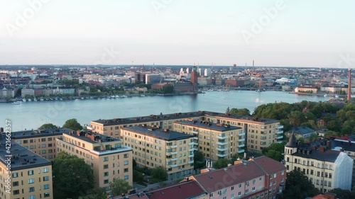 Late summer afternoon in Stockholm, Sweden. Aerial drone view from above rooftops, buildings, moving towards City Hall, Riddarfjärden, the sea of Mälaren, and the Old Town.