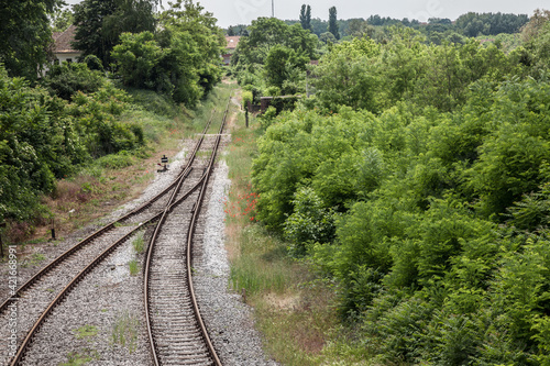 Panorama of old and rusty switch rail on an abandoned railway line with its typical metal track covered in grass and vegetals due to the lack of use