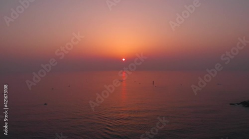 Sunrise at the east ocean with red glow sky. Red lighthouse stands on wave breaker at sea. Beautiful nature moment took with drone. 4K  