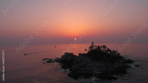 Sunrise at the east ocean with red glow sky. Aerial footage with small island with lighthouse at sea. Beautiful nature moment took with drone. 4K  