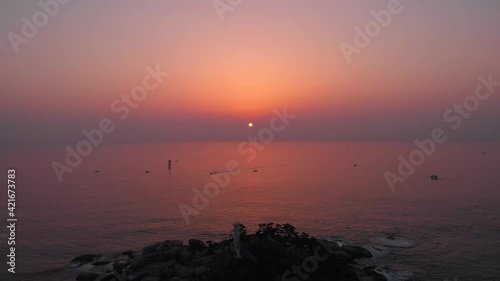 Sunrise at the east ocean with red glow sky. Aerial footage with small island with lighthouse at sea. Beautiful nature moment took with drone. 4K  