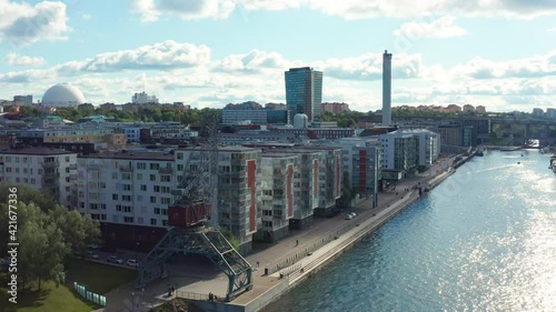 Stockholm, Sweden. Aerial Drone summer view of a beautiful boardwalk, canal and bay at Hammarby Sjöstad with modern architecture, marina, boats and an old container crane.