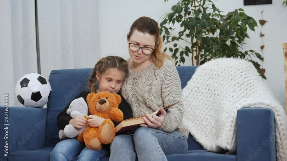 mom reads a lockdown book to her daughter at home. kid dream coronavirus stay home concept. mom is sitting on the couch with her daughter reading a book. mother and daughter happy family