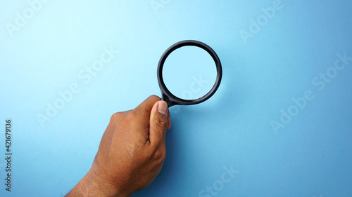 Man hand holding a magnifying glass on a blue background.
