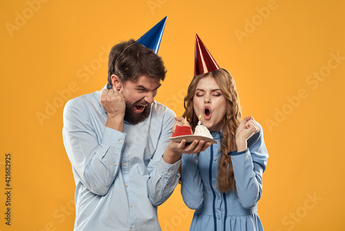 Birthday party man and woman on a yellow background in hats with a cake in their hands