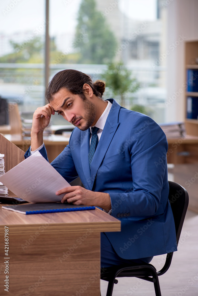 Young male employee unhappy with excessive work in the office Young male employee unhappy with excessive work in the office