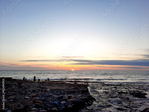 The river flows into the sea on a rocky beach against the backdrop of a sunset © German Ovchinnikov