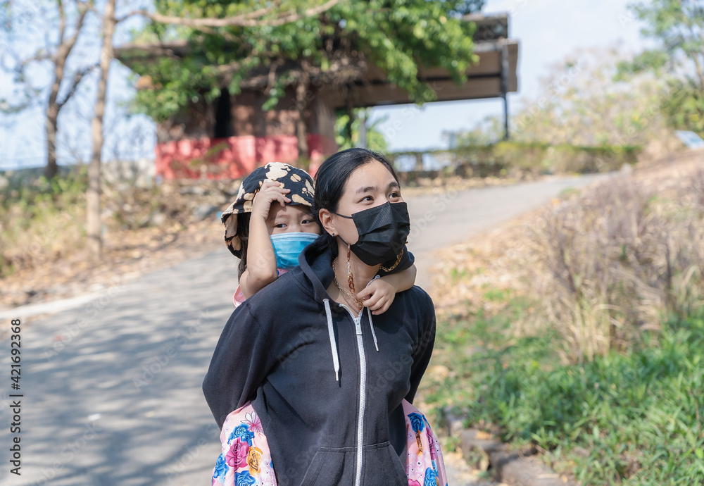 Young Asian woman and child girl wearing protective face mask to prevent coronavirus or COVID-19 pandemic disease symptoms during touring or walking in park with family.  Healthcare concept.