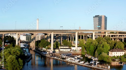 Stockholm, Scandinavia, Sweden. Aerial drone summer flying over bridges of lake Årstaviken , canal and bay in Södermalm with water, trees, marina, tower, chimney, cars, motor and sailing boats.