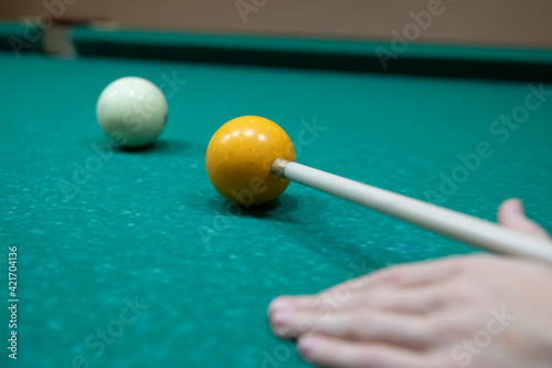 A man's hand hits a white billiard ball with a cue