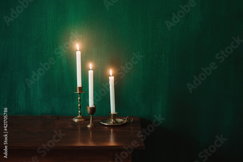 Fotografia 3 white candles on old gold candleholder on a wooden table and dark green wall
