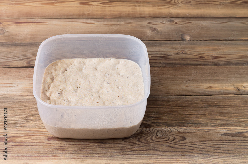 Rye sourdough on flour sourdough in a container on a wooden table. Fermentation.