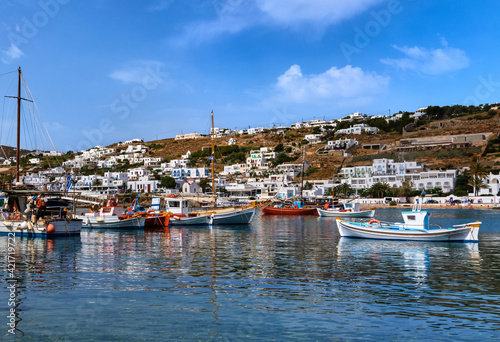 Beautiful summer day in Greek island port. Fishing boats, yachts moored at jetty. Small fishing boat in foreground. Mykonos, Cyclades, Greece.