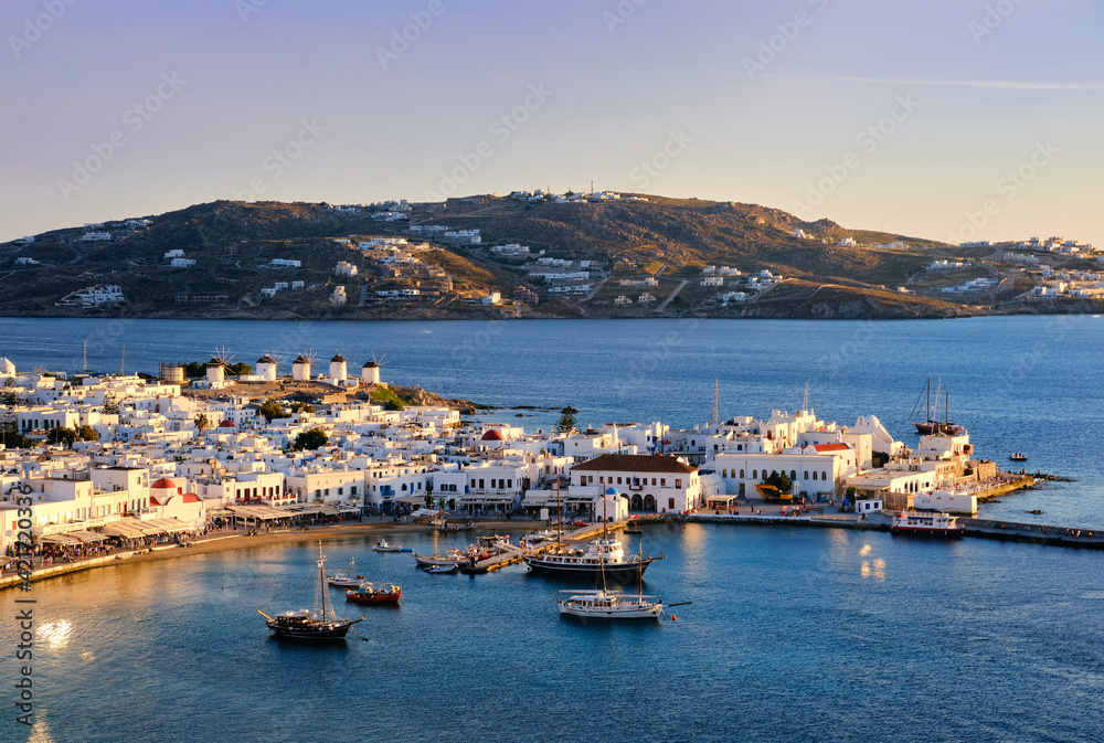 Beautiful sunset view over Mykonos, Cyclades, Greece, harbor and port. Golden hour, ships, whitewashed houses. Vacations, Mediterranean lifestyle.